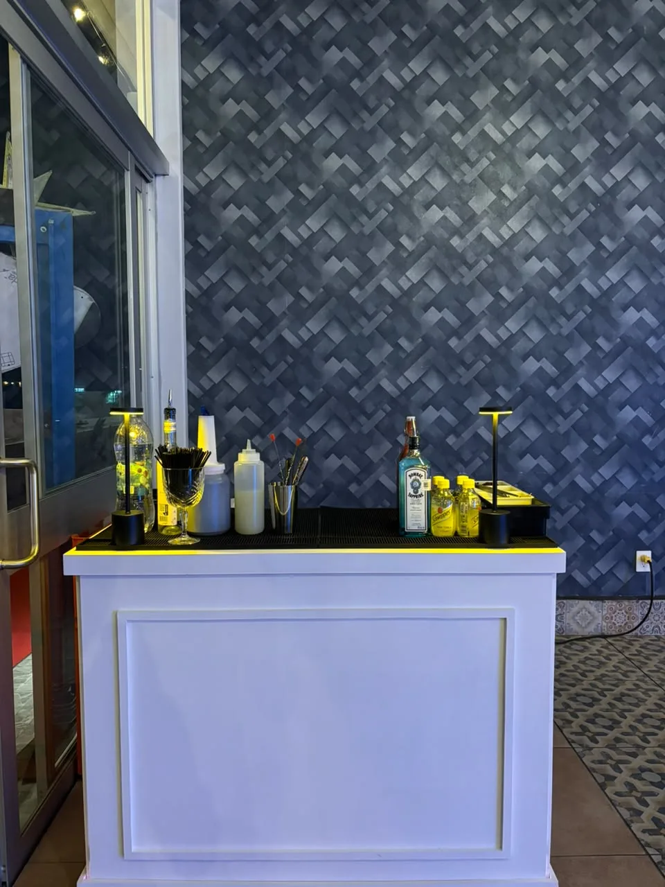 Barra Caval blanca con luz LED, lámparas y botellas de gin en un salón