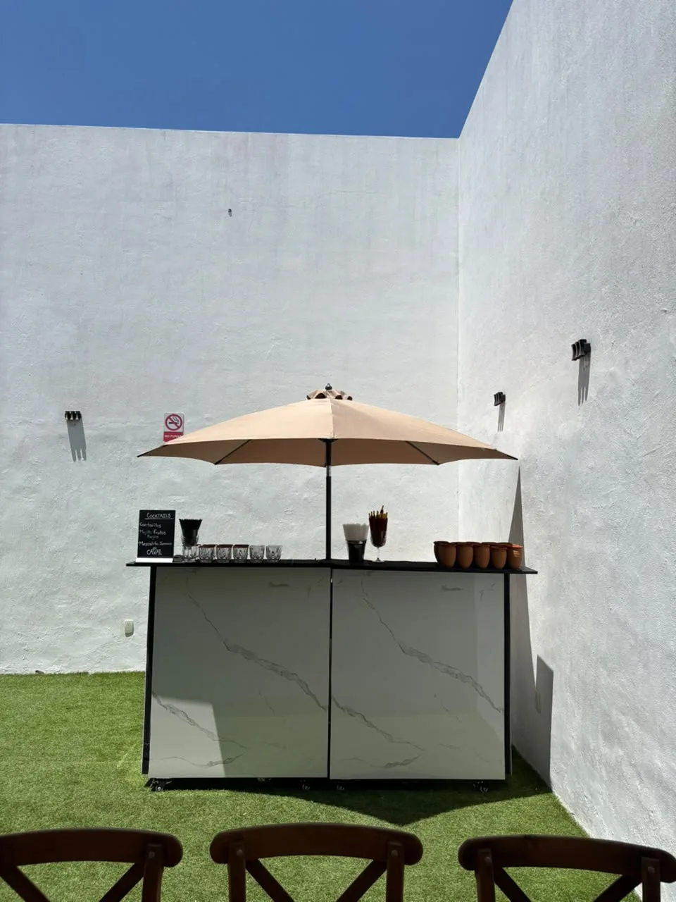 Barra Caval de mármol con sombrilla en un jardín, con jarritos de barro y pizarra de cocteles